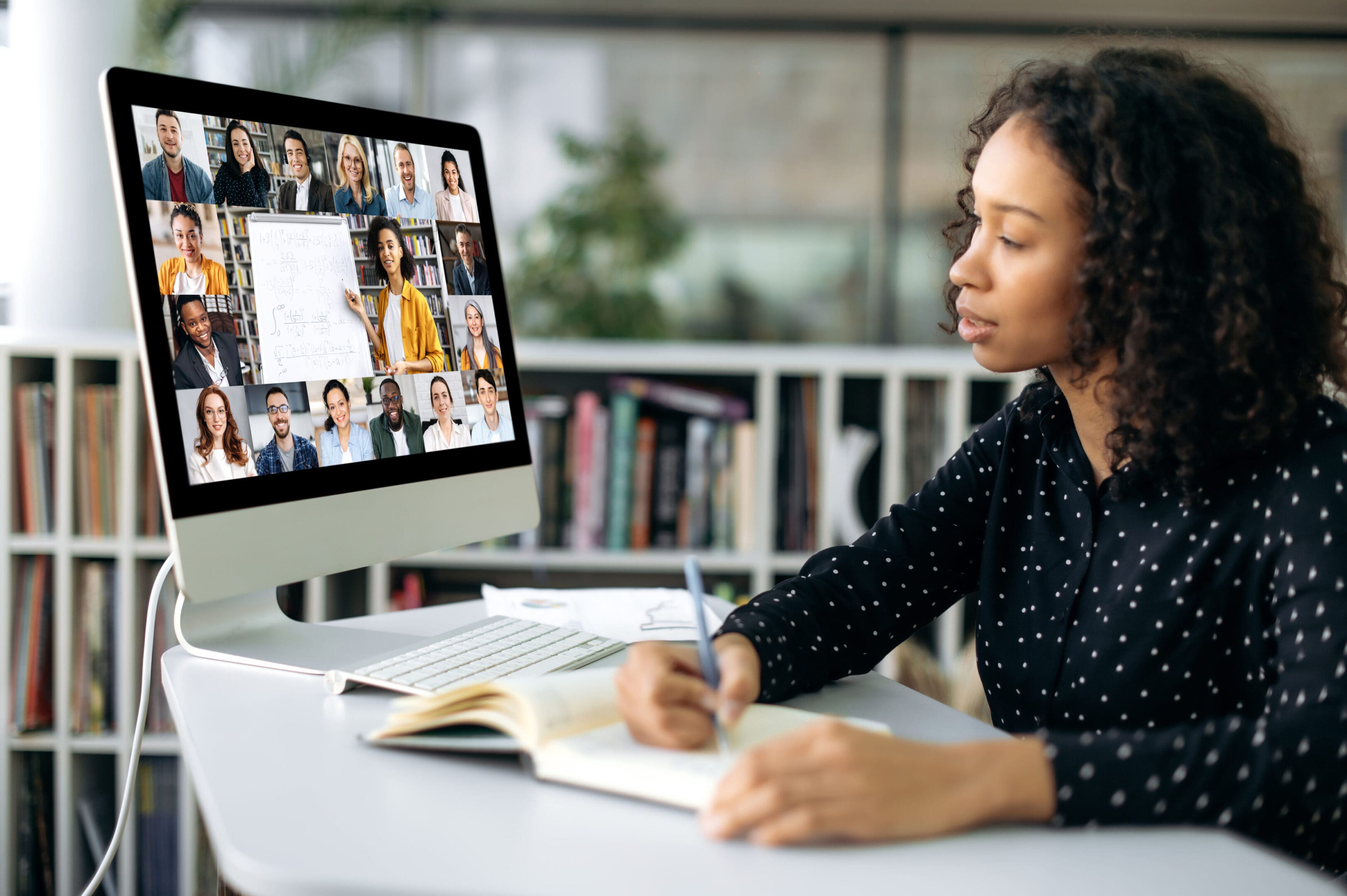 Woman multitasking with video call and note-taking in a modern workspace.